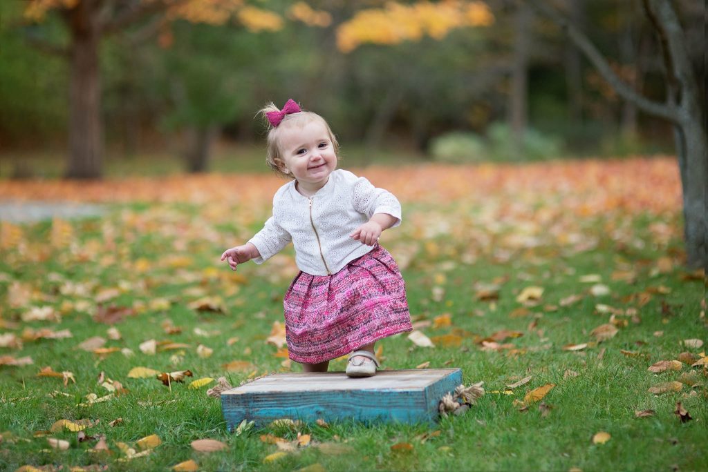 Baby girl stepping up on blue box on the grass