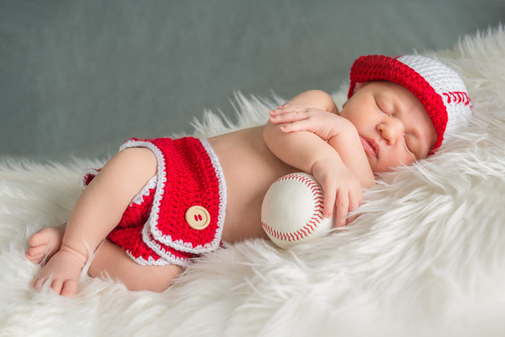 baby sleeping with baseball on white blanket