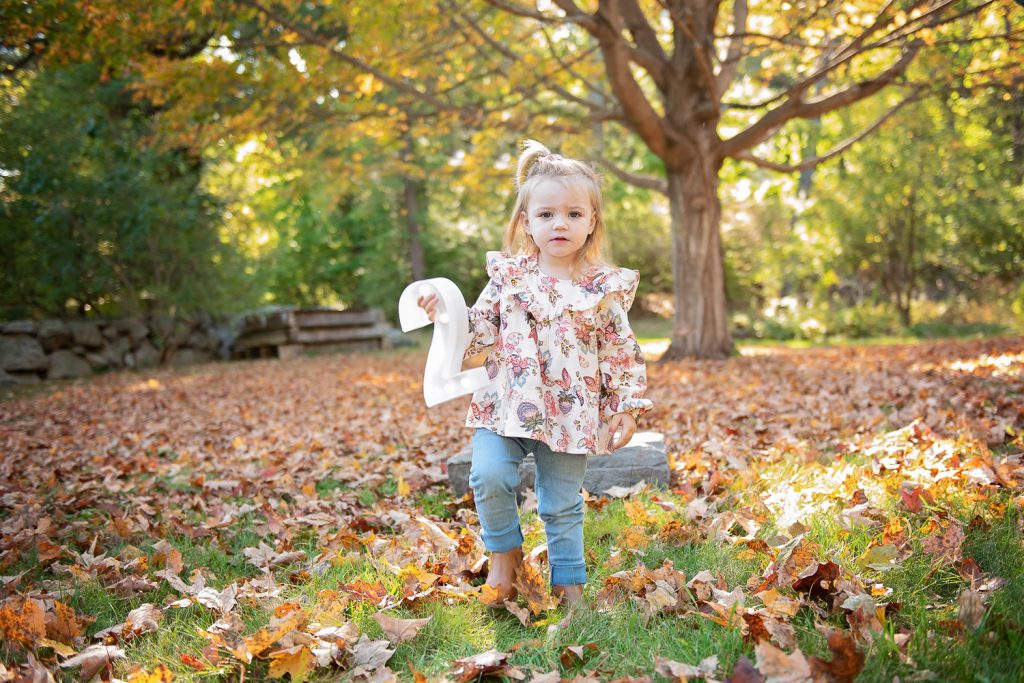 a girl standing in the grass with leaves and a number two