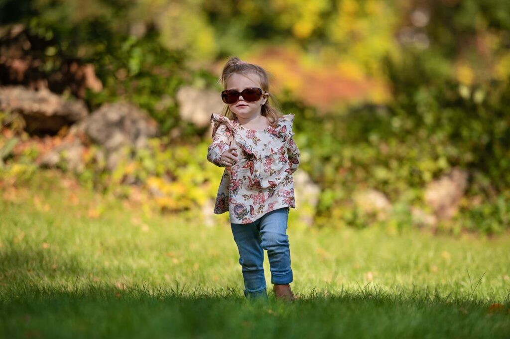 a little girl wearing sunglasses and walking in grass