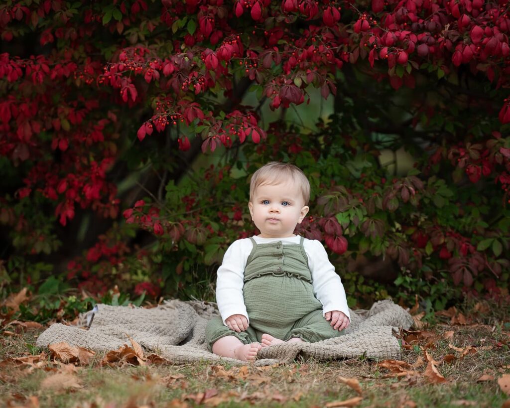 a baby sitting on a blanket under a tree